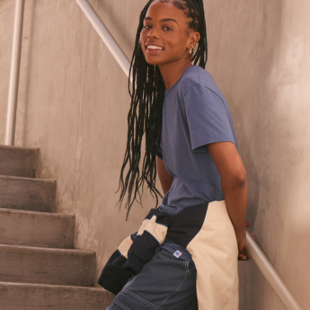 Female model wearing a blue short sleeve Russell Tee with jacket tied around waist.